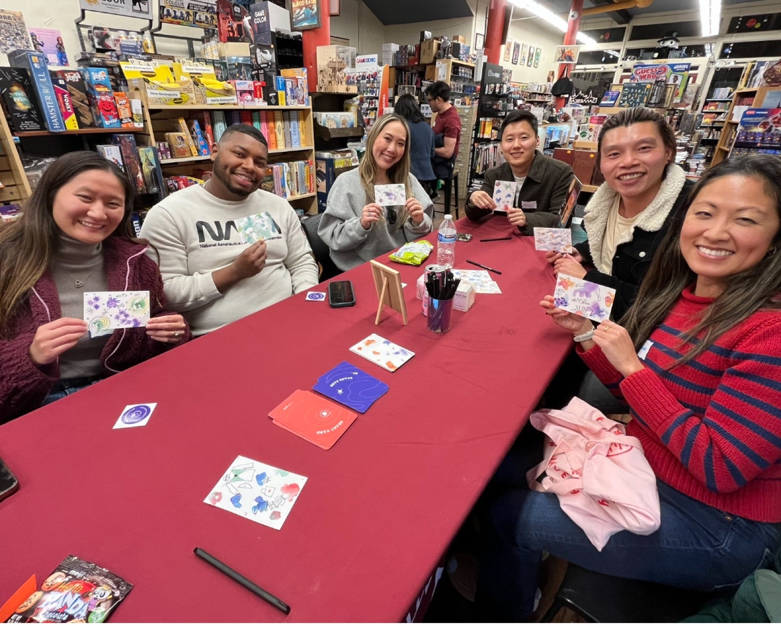 A table of players at a game store holding up their doodled blob cards