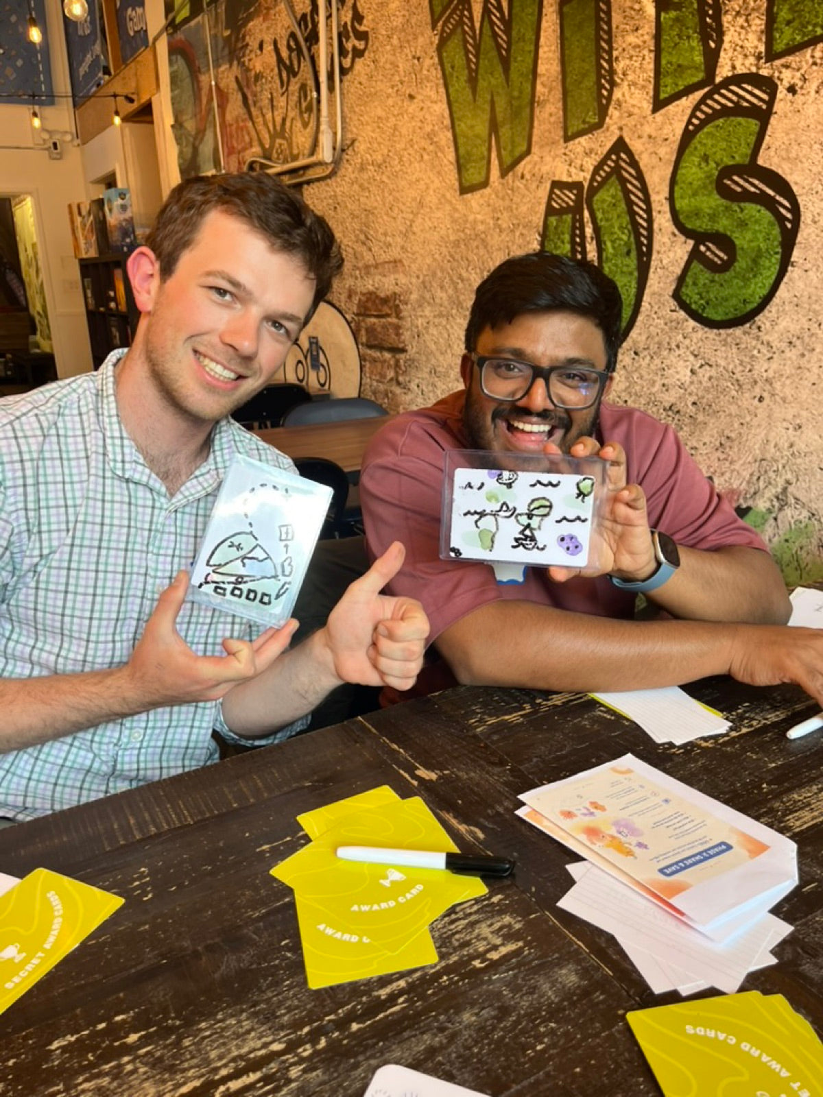 A table of players at a game store holding up their doodled blob cards